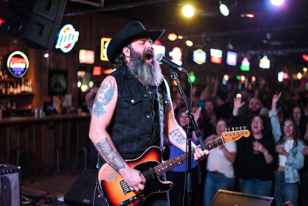 Bearded singer performing on stage in a packed bar